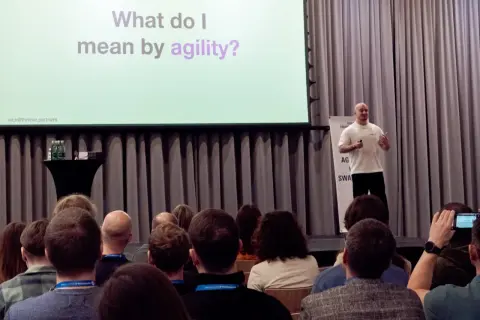 Prelegent wyjaśnia, co to agile, podczas konferencji. Na ekranie pytanie: "What do I mean by agility?".