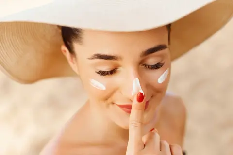 Mujer con sombrero de ala ancha se aplica protector solar en su piel blanca.