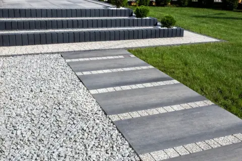 Nowoczesny chodnik z płyt betonowych i kamyczków, prowadzący do schodów.