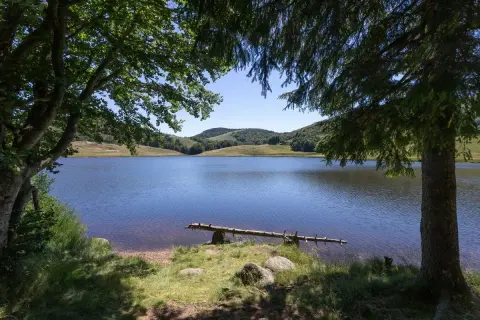 Calme et serein, le lac des Pises reflète le ciel bleu. Des arbres ombragent ses rives verdoyantes.