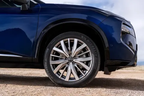 Błękitny Nissan X-Trail na drodze gruntowej, z widocznym kołem i fragmentem nadwozia.