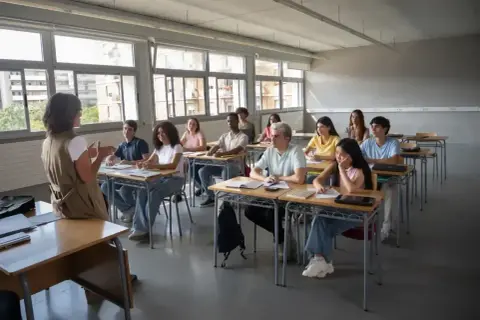 Nauczycielka prowadzi lekcję wychowania do życia w rodzinie. Uczniowie uważnie słuchają, siedząc w ławkach.