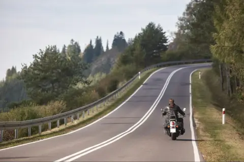 Motocyklista na zakręcie górskiej drogi, otoczony drzewami.