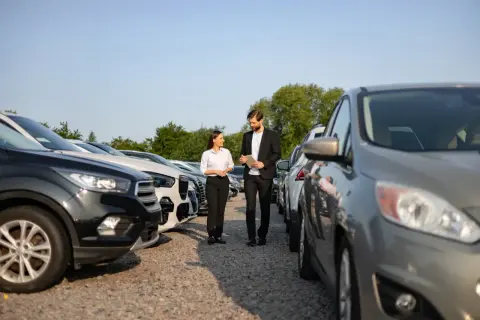 Para omawia na placu samochodowym kwestie amortyzacji środków trwałych, analizując flotę pojazdów.