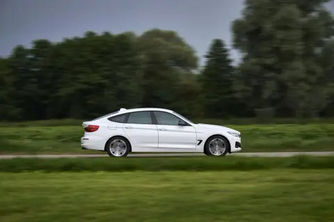 Białe BMW 330d mija zielone pola i drzewa, poruszając się z dużą prędkością.