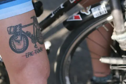Tatuaż rowerowy z napisem "EPIC TOUR" na ramieniu rowerzysty.