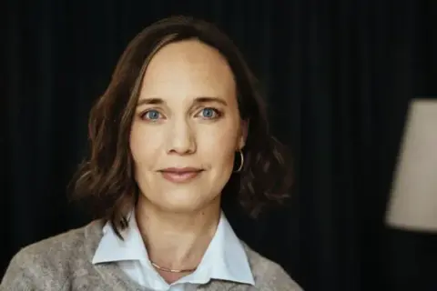 Kvinna med blå ögon och brunt hår, klädd i kofta och skjorta. Hon ser ut att ha en tankfull blick, kanske funderar hon på relations-ocd.