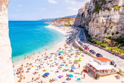 Spiagge vicino Tropea affollate di bagnanti sotto scogliere imponenti. Acqua cristallina e case colorate a picco sul mare.