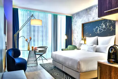 Nowoczesny pokój w hotelu NYX Warszawa: łóżko z białym pościelą, stolik kawowy, granatowe fotele i zielona sofa.