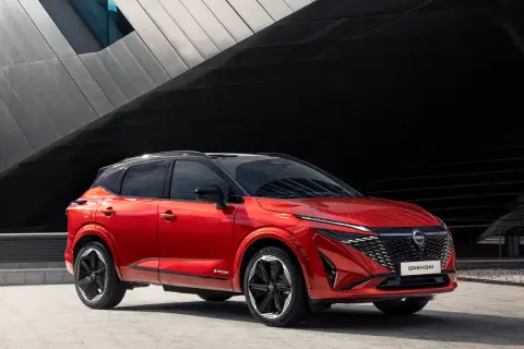 Czerwony Nissan Qashqai prezentuje swoje nowoczesne linie i imponujące nissan qashqai wymiary. Stylowy SUV na tle architektonicznej fasady.