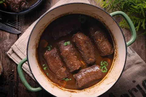 Rinderrouladen im Backofen schmorend in dunkler Sauce, garniert mit Petersilie. Ein rustikales Gericht, das Wärme und Genuss verspricht.