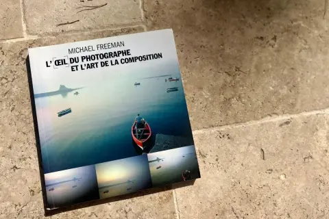 L'œil du photographe et l'art de la composition, un livre de Michael Freeman, présente des paysages marins paisibles avec des bateaux et un îlot lointain.
