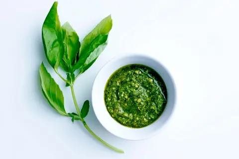 Färskt basilika bredvid en skål med hemlagad pesto. Ett perfekt pesto recept för sommaren.