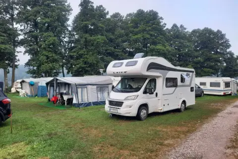 Kampery i przyczepy kempingowe na trawiastym polu, w tle drzewa. Widać namioty i meble ogrodowe. To idealne miejsce na wypoczynek w camp park sonata.