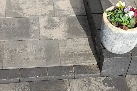 Różne rodzaje kostki brukowej tworzą elegancką ścieżkę. Jasnoszara i grafitowa kostka brukowa, z ozdobną donicą z kwiatami.