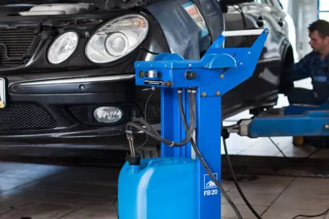 Mechanik przeprowadza wymianę płynu hamulcowego w czarnym samochodzie, używając specjalistycznego sprzętu.