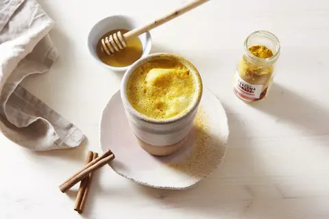 Un golden latte crémeux, prêt à déguster. Découvrez les golden latte bienfaits pour une pause réconfortante et saine. Miel et curcuma à portée de main.