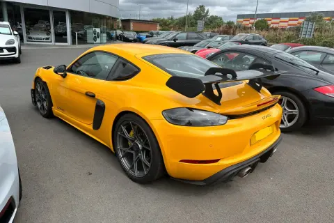 Żółty Porsche GT4 RS z dużym spojlerem, gotowy do wyścigów samochodowych, zaparkowany obok czarnych aut.