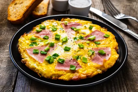 Pyszny omlet z szynką i serem, posypany szczypiorkiem, podany z grzankami. Idealny na śniadanie.