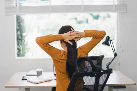 Person sträcker på sig vid ett skrivbord, en paus för att arbeta ergonomiskt.
