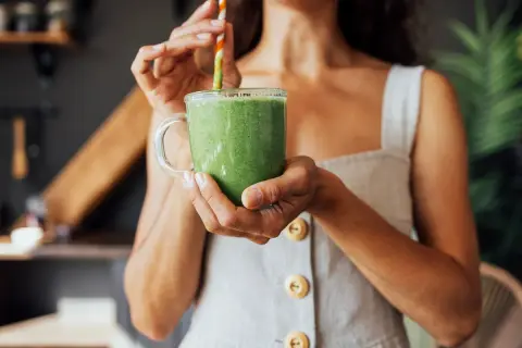 Donna sorseggia un frullato verde, un'ottima opzione su cosa bere per dimagrire.