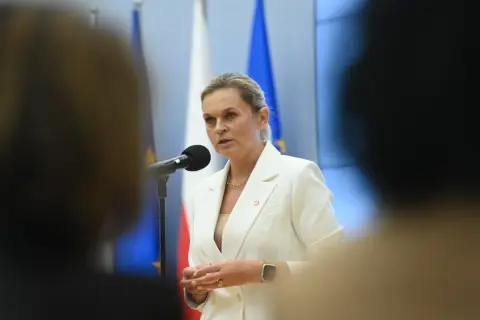 Minister edukacji przemawia przy mikrofonie, w tle flagi Polski i UE.