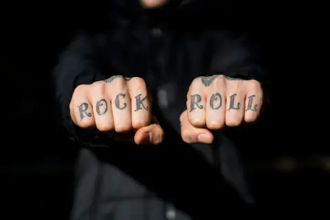 Manos con tatuajes en los nudillos que dicen "ROCK ROLL". A pesar de la pena y el pánico, el rock and roll vive.