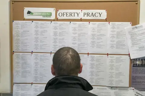 Mężczyzna przegląda tablicę z ofertami pracy w Powiatowym Urzędzie Pracy. Może szukać pracy, która zapewni mu godną kuroniówkę.