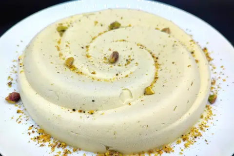 Delizioso semifreddo al pistacchio, decorato con granella e pistacchi interi, servito su un piatto bianco.
