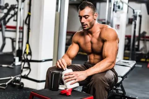 Muskulöser Mann im Fitnessstudio bereitet Proteinshake zu. Was hilft beim Muskelaufbau? Richtige Ernährung und Supplemente sind wichtig.