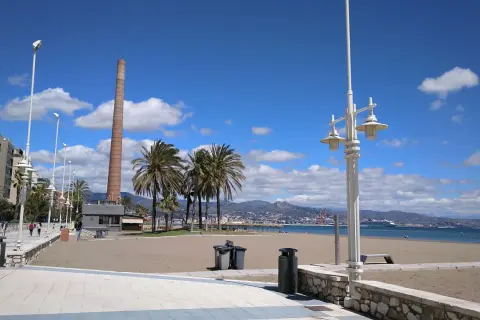 Paseo marítimo con palmeras y chimenea industrial. La playa Misericordia, ideal para llegar y disfrutar del mar.