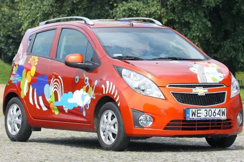Pomarańczowy Chevrolet Spark 2010 z kolorowymi, abstrakcyjnymi wzorami na karoserii.