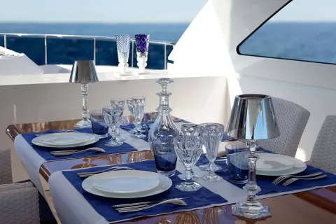 Un dîner élégant sur un yacht, avec des verres en cristal, des carafes et les différents couverts de table disposés sur des nappes bleues.