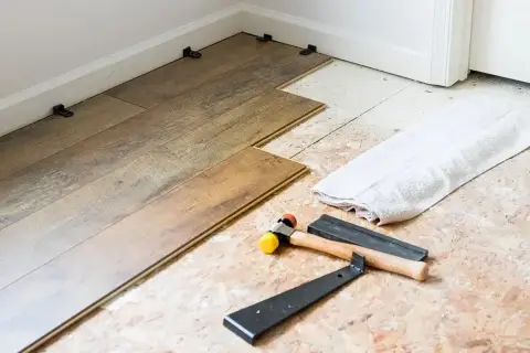Laying LVP flooring parallel to the longest wall is a common practice. Tools like a rubber mallet and pry bar are ready for installation.
