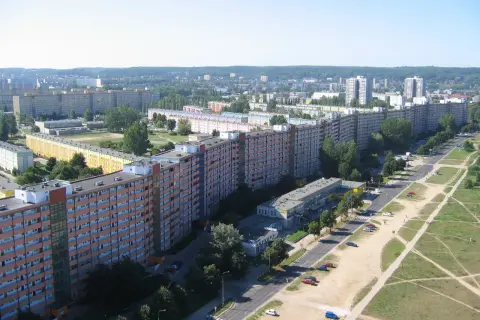 Długi falowiec gdański wzdłuż ulicy, z wieloma oknami i balkonami, otoczony zielenią i innymi budynkami.