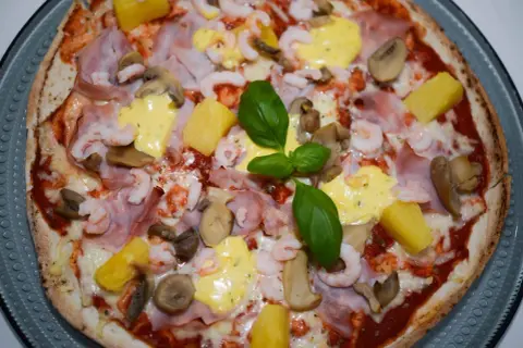 En läcker pizza med räkor och skinka, toppad med ananas, champinjoner och en krämig sås. En riktig smakupplevelse!