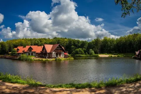 Idealne miejsce na długi weekend w sierpniu: urokliwe domki nad jeziorem, otoczone lasem, z pięknym niebem i chmurami.