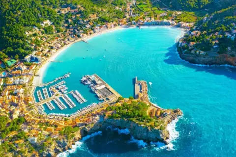 Vacker vy över en turkos bukt med en hamn full av båtar och en stad som klättrar uppför kullarna. En drömsemester i Palma de Mallorca.