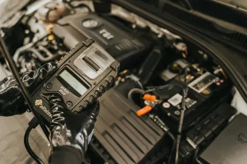 Rękawiczki mechanika pokazują tester akumulatorów, gotowy do sprawdzenia, jak naładować akumulator w samochodzie.