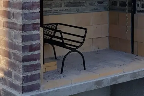 En påbörjad grill av tegelstenar med en svart metallbänk inuti.