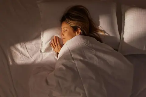 A woman sleeps peacefully, her hands clasped. The image captures the quiet stillness of sleep, hinting at the subtle rhythm of her respiratory rate while sleeping.