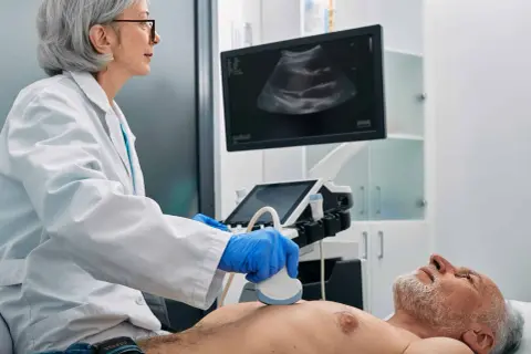 Ärztin führt Ultraschalluntersuchung durch. Der Bildschirm zeigt ein Bild, das auf eine Untersuchung von Organen oder Lymphknoten hindeutet.