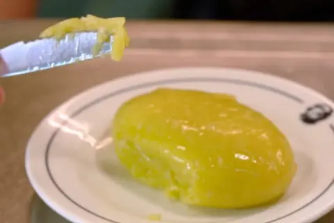 Un trozo de alioli casero untado en un cuchillo, listo para probar la deliciosa salsa sobre un plato blanco.
