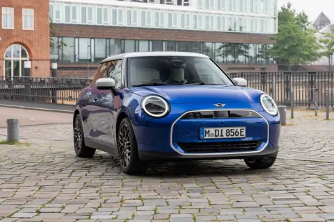 Mini Cooper SE azul aparcado en calle adoquinada, con edificios modernos de fondo. Su autonomía eléctrica inspira libertad.