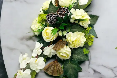 Eleganckie kompozycje funeralne z białych róż, storczyków i ozdobnych łusek lotosu na marmurowym tle.