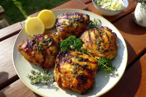 Grillad, saftig marinera kyckling med örter och citronklyftor på en tallrik. Perfekt sommarmat!