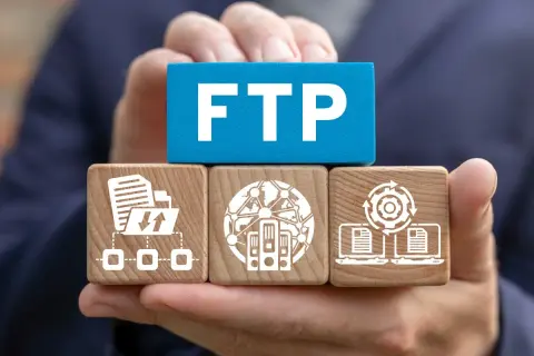 Ręce trzymają klocki symbolizujące transfer plików przez ftp: folder z ikonami pobierania/wysyłania, serwery w sieci, laptopy z dokumentami i mechanizmem.