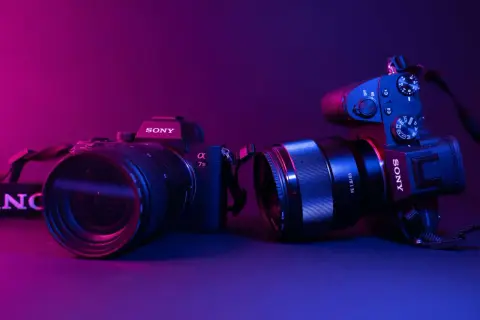 Dwa aparaty Sony, jeden z obiektywem 70-200mm, drugi z 85mm f/1.8. Różne rodzaje aparatów fotograficznych w neonowym świetle.