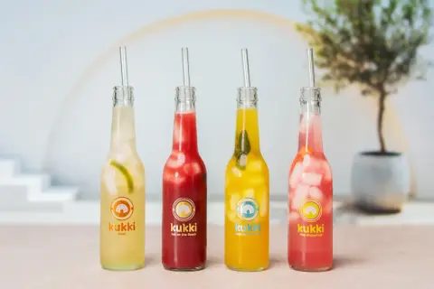 Vier bunte Kukki Cocktails mit Eis und Strohhalmen, bereit zum Auftauen und Genießen.