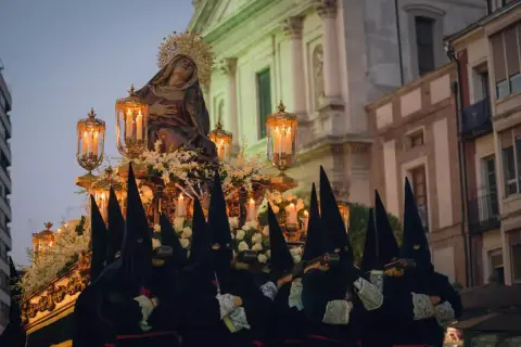 Figuras encapuchadas portan un paso con la Virgen, iluminado por velas, durante las procesiones de Sábado Santo.
